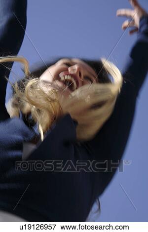 Stock Photo - Young blond woman dancing, jumping and cheering at the beach, worm's eye view. Fotosearch