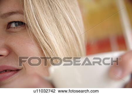 Stock Image - Young blond woman holding a cup, face detail. Fotosearch
