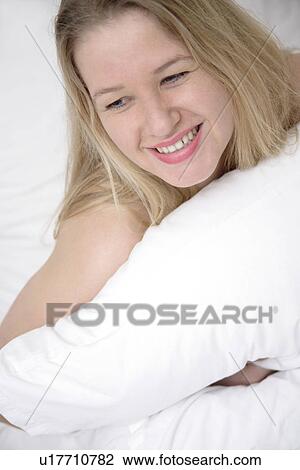 Stock Image - Young blond woman sitting up in bed, laughing. Fotosearch