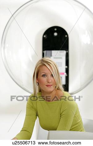 Stock Image - Young business woman sitting in a modern hotel lounge, public phone in background. Fotosearch