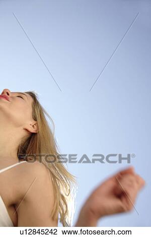 Stock Image - Young woman in a happy mood in front of blue sky, view from below. Fotosearch