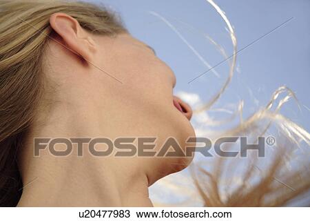 Stock Image - Young woman in a happy mood in front of blue sky, view from below. Fotosearch