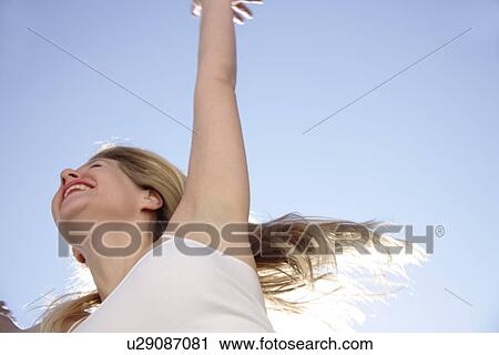 Stock Image - Young woman in a happy mood in front of blue sky, view from below. Fotosearch