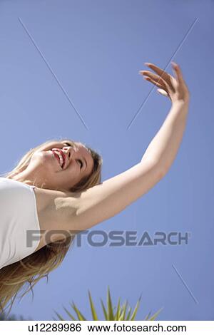 Young woman in a happy mood in front of blue sky, view from below View Large Photo Image Stock Photograph - Young woman in a happy mood in front of blue sky, view from below. Fotosearch