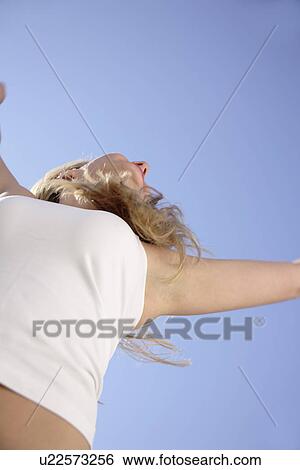 Young woman in a happy mood in front of blue sky, view from below View Large Photo Image Stock Photograph - Young woman in a happy mood in front of blue sky, view from below. Fotosearch