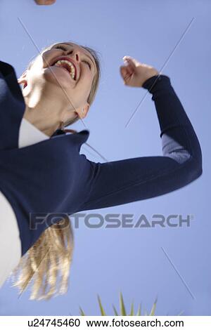 Young woman jumping happily in front of blue sky, view from below View Large Photo Image Stock Image - Young woman jumping happily in front of blue sky, view from below. Fotosearch
