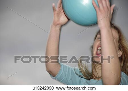 Stock Image - Young woman playing with a ball at the beach. Fotosearch