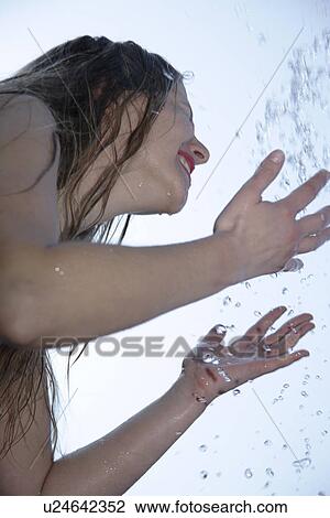 Stock Image - Young woman refreshing herself by splashing water all over her body, low angle view, close up. Fotosearch