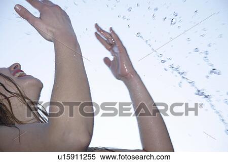 Stock Photography - Young woman refreshing herself by splashing water all over her body, low angle view, close up. Fotosearch