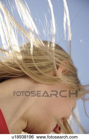 Stock Photograph - Young woman throwing her long blond hair in front of blue sky, low angle view. Fotosearch