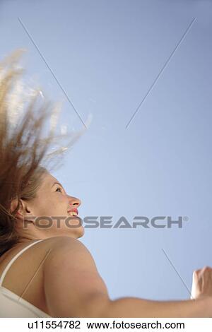 Stock Image - Young woman tossing her long blond hair in front of blue sky, view from below. Fotosearch