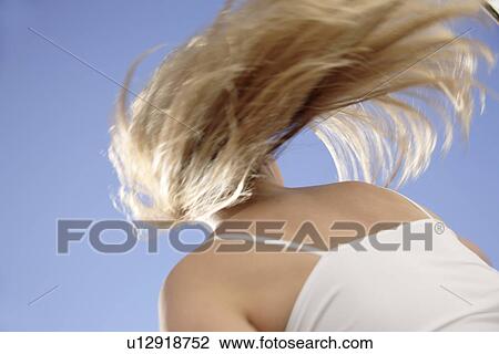 Stock Image - Young woman tossing her long blond hair in front of blue sky, view from below. Fotosearch