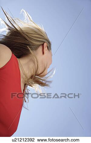 Stock Image - Young woman tossing her long blond hair in front of blue sky, view from below. Fotosearch
