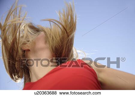 Stock Photo - Young woman tossing her long blond hair in front of blue sky, view from below. Fotosearch