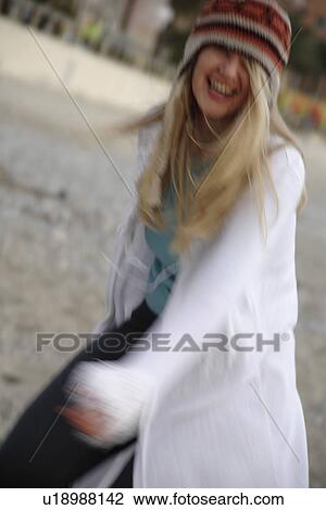 Stock Image - Young woman wearing knitted cap, walking at the beach, smiling. Fotosearch