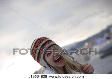 Stock Photo - Young woman wearing knitted cap, running and laughing at the beach, close up. Fotosearch