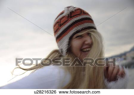 Stock Photograph - Young woman wearing knitted cap, running and laughing at the beach, close up. Fotosearch