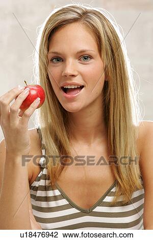 Stock Image - Young woman with long blond hair eating an apple, portrait. Fotosearch