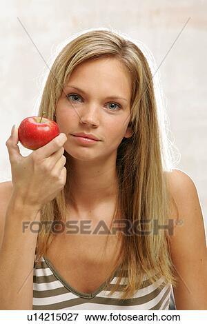 Stock Photo - Young woman with long blond hair eating an apple, portrait. Fotosearch