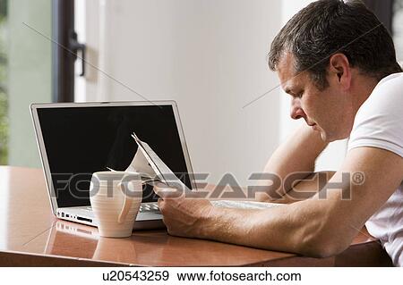 Stock Photo - Man Reading Newspaper with Laptop and Coffee. Fotosearch