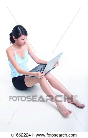 Stock Image - Young woman sitting and using notebook. Fotosearch
