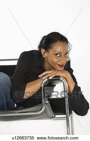 Stock Photography - African American mid-adult woman lounging in chair smiling and looking at viewer.. Fotosearch