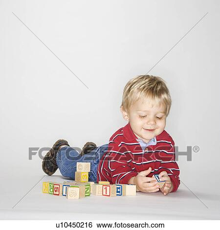 Stock Photograph - Boy lying on stomach propped up on elbows playing with toy blocks. Fotosearch