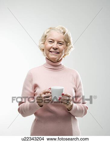 Picture - Caucasian senior woman holding coffee cup smiling at viewer.. Fotosearch