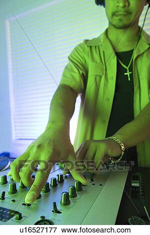 Stock Photo - Close-up of young adult male DJ with hand on control panels of mixing equipment. Fotosearch