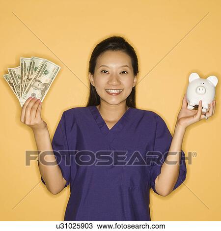 Stock Image - Doctor holding piggy bank in one hand and cash in the other . Fotosearch