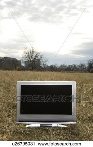 Stock Image - Flat screen television set in grassy field. Fotosearch
