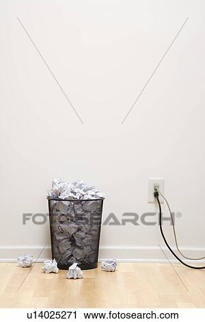 Stock Image - Full wire mesh trash can with crumpled paper next to electrical outlet and plugs. Fotosearch