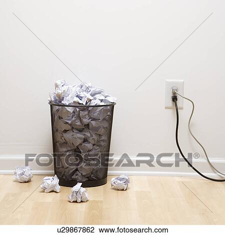 Stock Image - Full wire mesh trash can with crumpled paper next to electrical outlet and plugs. Fotosearch