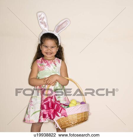 Stock Image - Girl wearing bunny ears holding Easter basket smiling . Fotosearch