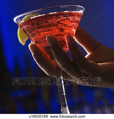 Stock Photo - Male hand holding martini in bar against glowing blue background. Fotosearch
