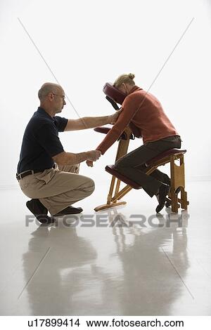 Picture - Male massage therapist massaging arms and hands of woman sitting in massage chair. Fotosearch