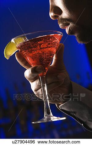 Stock Photograph - Man bringing martini up to lips in bar . Fotosearch
