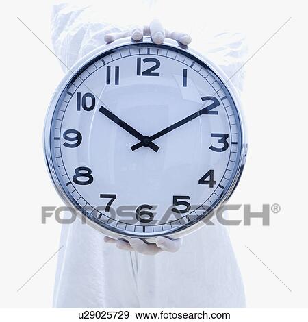 Stock Photo - Man in biohazard suit holding out clock standing . Fotosearch