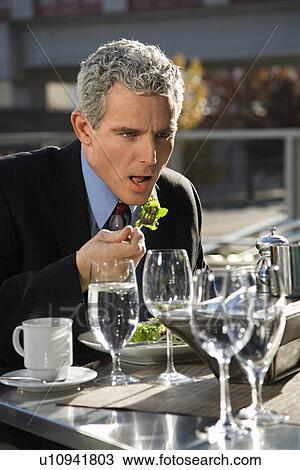 Man sitting at outside patio table eating salad View Large Photo Image Stock Image - Man sitting at outside patio table eating salad. Fotosearch
