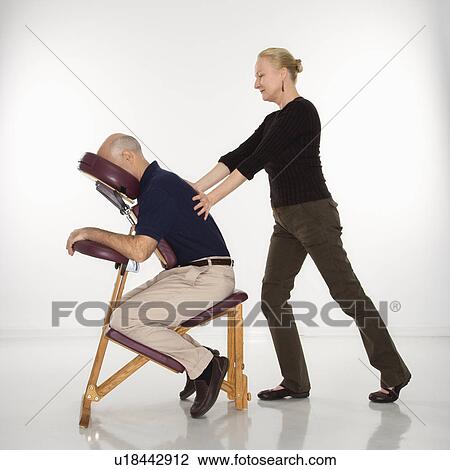 Stock Image - Massage therapist massaging back of man sitting in massage chair. Fotosearch