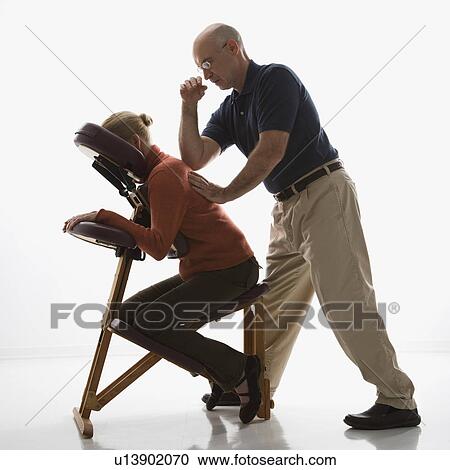 Stock Image - Massage therapist massaging back of woman sitting in massage chair. Fotosearch