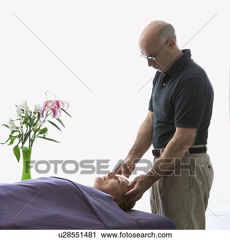 Stock Image - Massage therapist massaging face of woman lying on massage table. Fotosearch