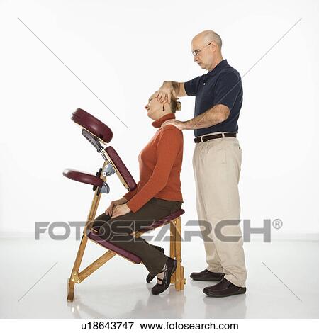 Stock Photo - Massage therapist massaging neck of woman sitting in massage chair. Fotosearch