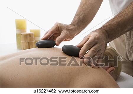 Stock Image - Massage therapist placing hot stones on back of woman. Fotosearch