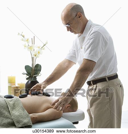 Massage therapist placing hot stones on back woman lying on massage table View Large Photo Image Stock Photo - Massage therapist placing hot stones on back woman lying on massage table. Fotosearch