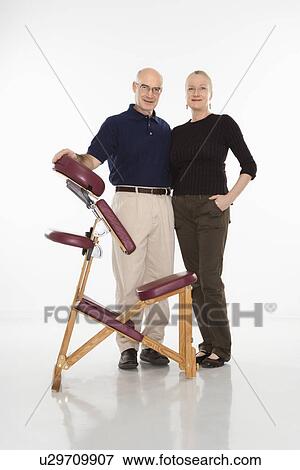 Stock Photo - Massage therapist standing with arm around woman beside massage chair. Fotosearch