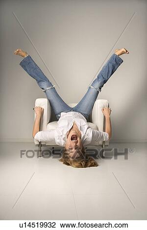 Mid-adult woman in blue jeans lying upside down on chair with legs in air laughing View Large Photo Image Stock Image - Mid-adult woman in blue jeans lying upside down on chair with legs in air laughing. Fotosearch