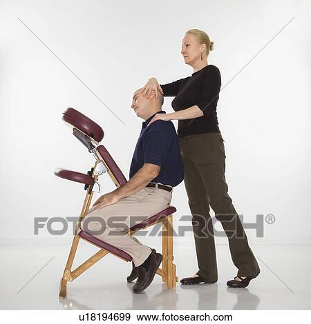 Middle-aged female massage therapist massaging neck of middle-aged man sitting in massage chair View Large Photo Image Stock Photo - Middle-aged female massage therapist massaging neck of middle-aged man sitting in massage chair. Fotosearch