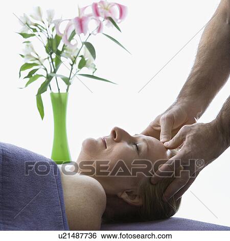 Middle-aged male massage therapist massaging temples of middle-aged woman laying on massage table View Large Photo Image Stock Photograph - Middle-aged male massage therapist massaging temples of middle-aged woman laying on massage table. Fotosearch