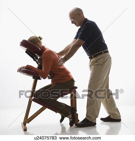 Middle-aged massage therapist massaging back of middle-aged woman sitting in massage chair. View Large Photo Image Stock Image - Middle-aged massage therapist massaging back of middle-aged woman sitting in massage chair. . Fotosearch